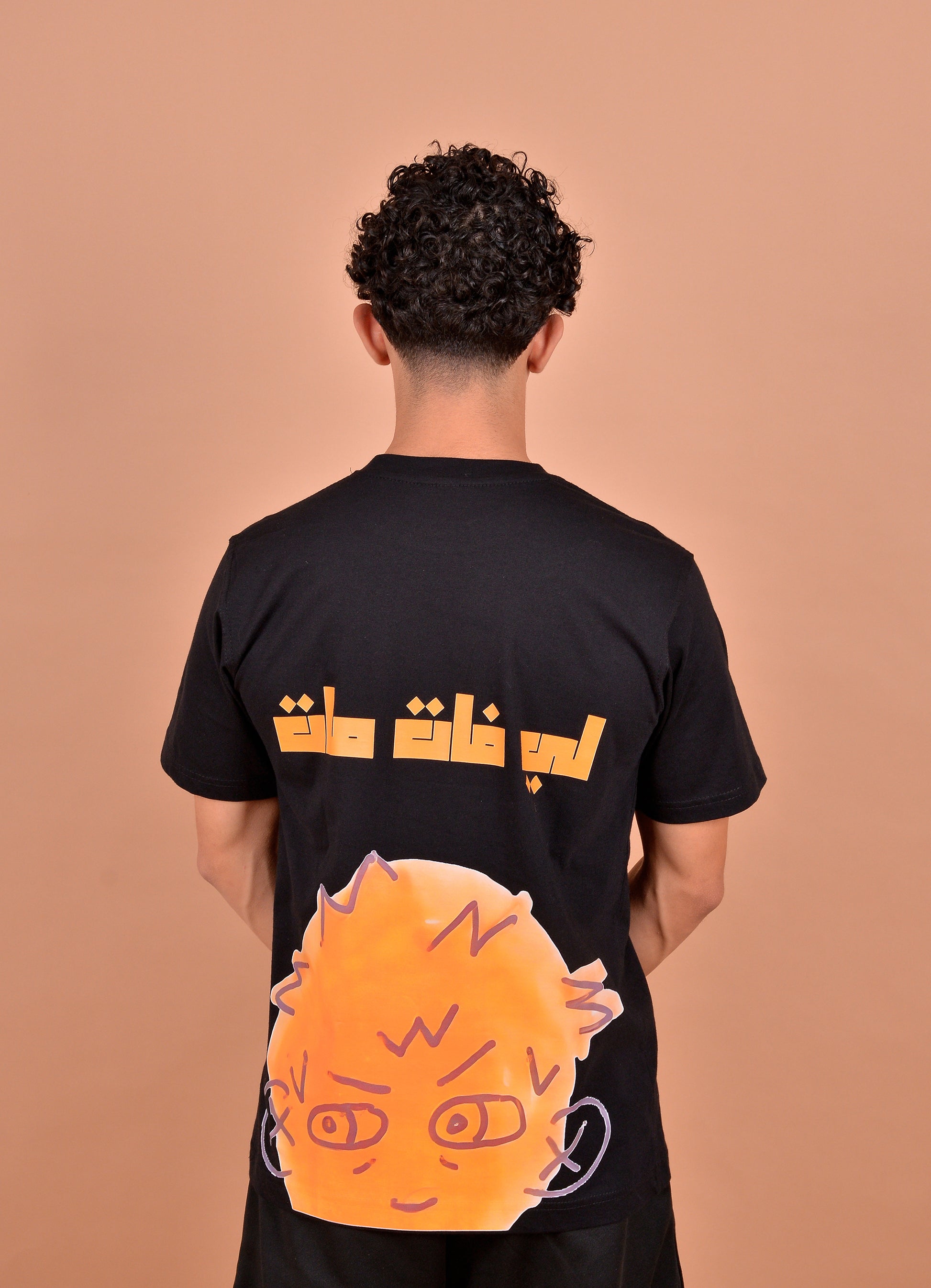 Person wearing a black t-shirt with orange and white graphics on a brown background