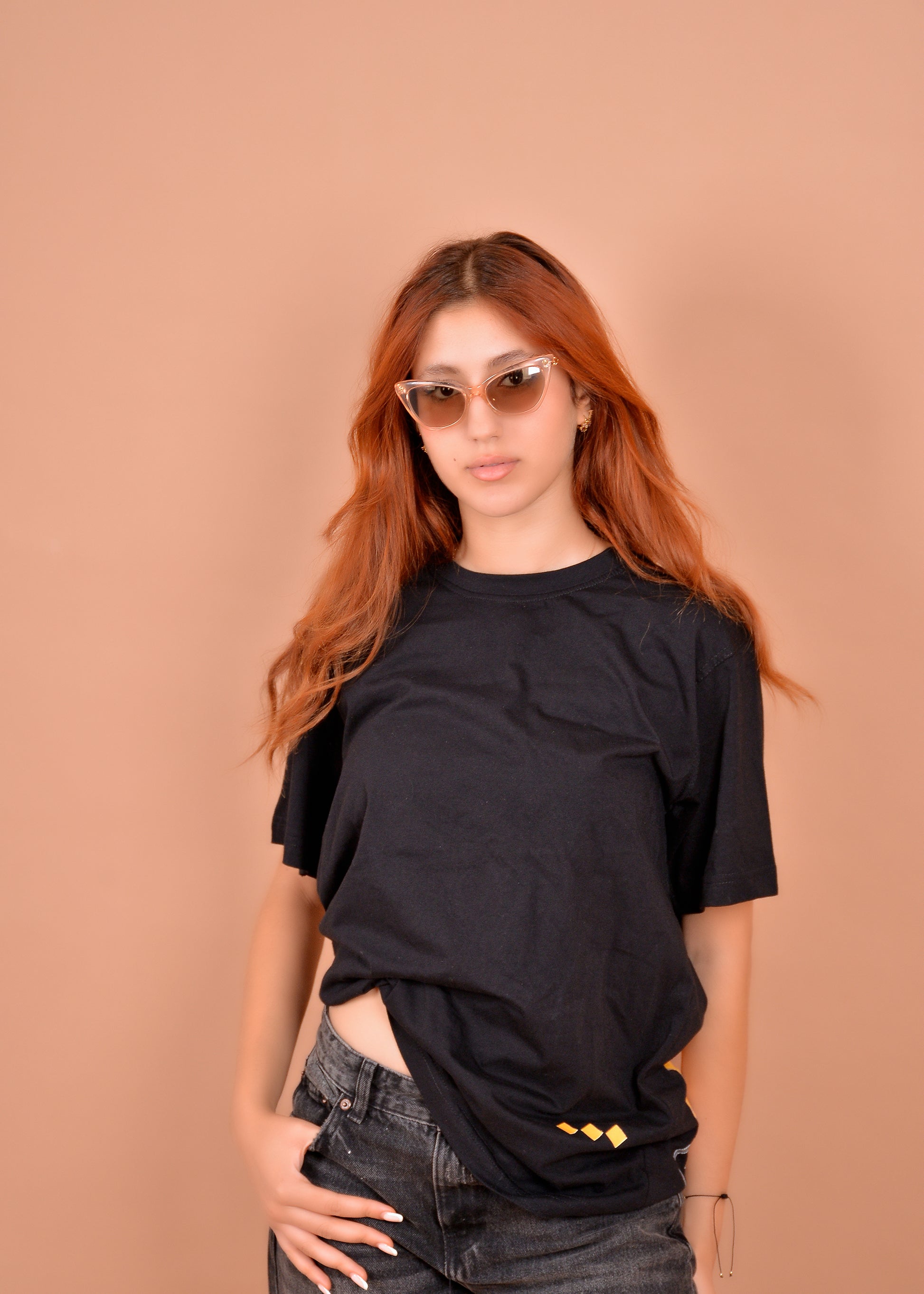 Person wearing a black oversized t-shirt and sunglasses against a beige background