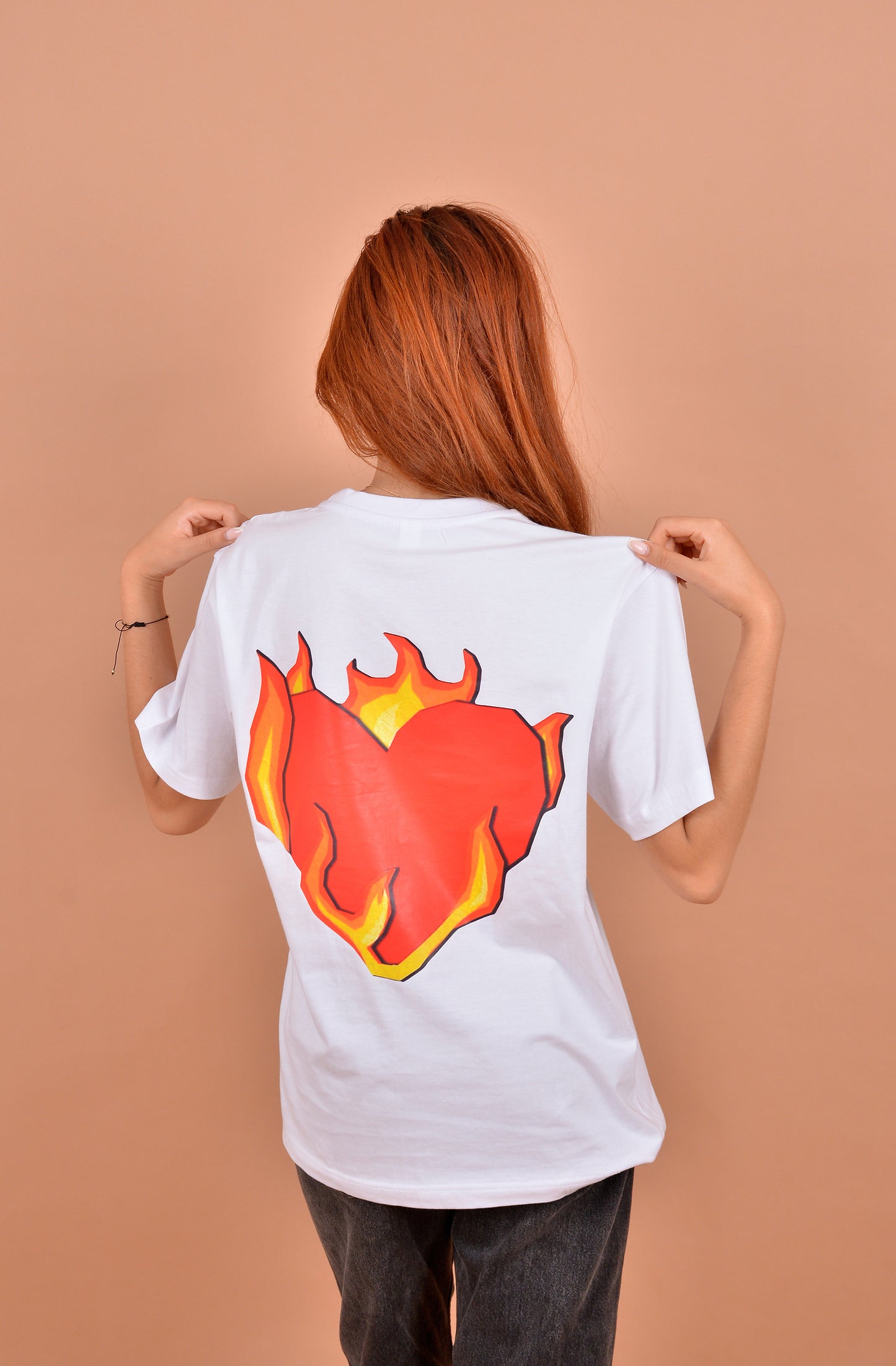 Person wearing a white t-shirt with a red heart design on the back against a beige background